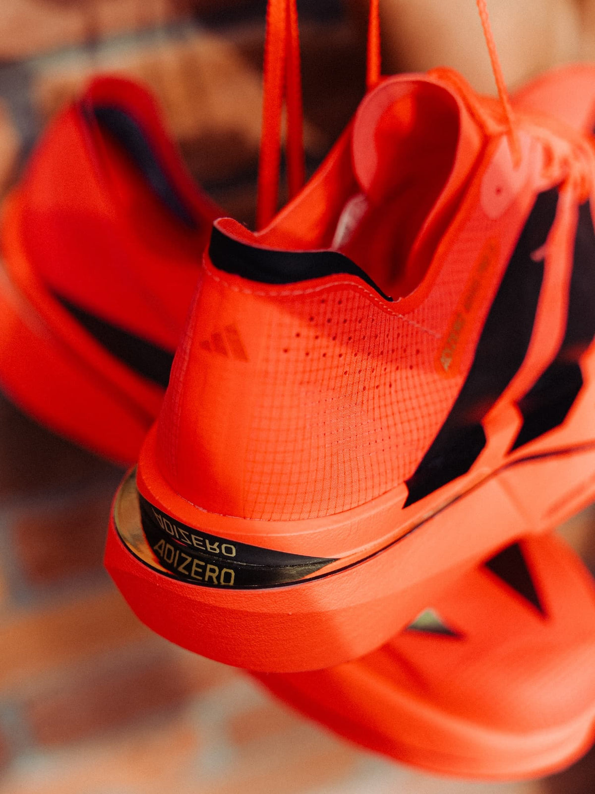Close-up of a bright orange Adidas Adios Pro 5 running shoe, showing the heel and midsole reflective Adizero detail.