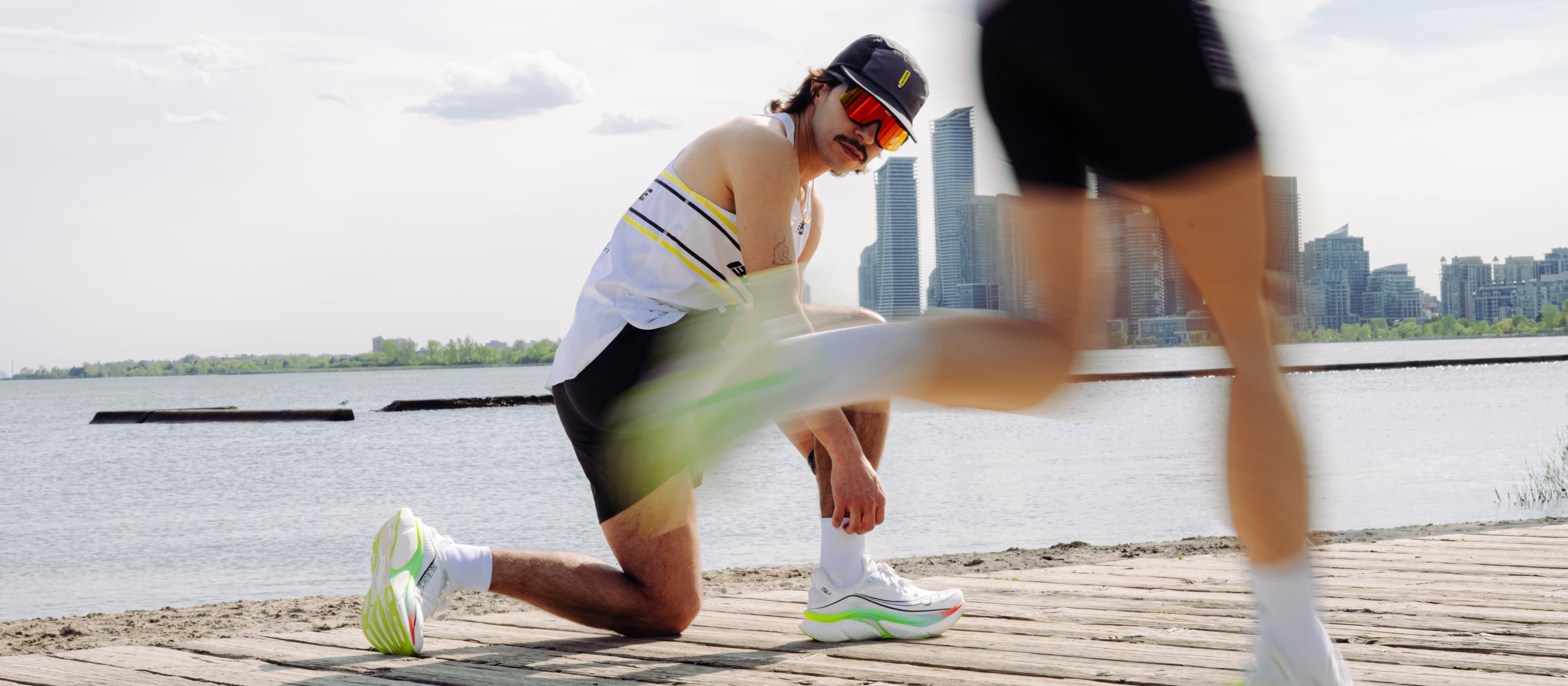 Two runners stretching on a dock with city skyline in the background